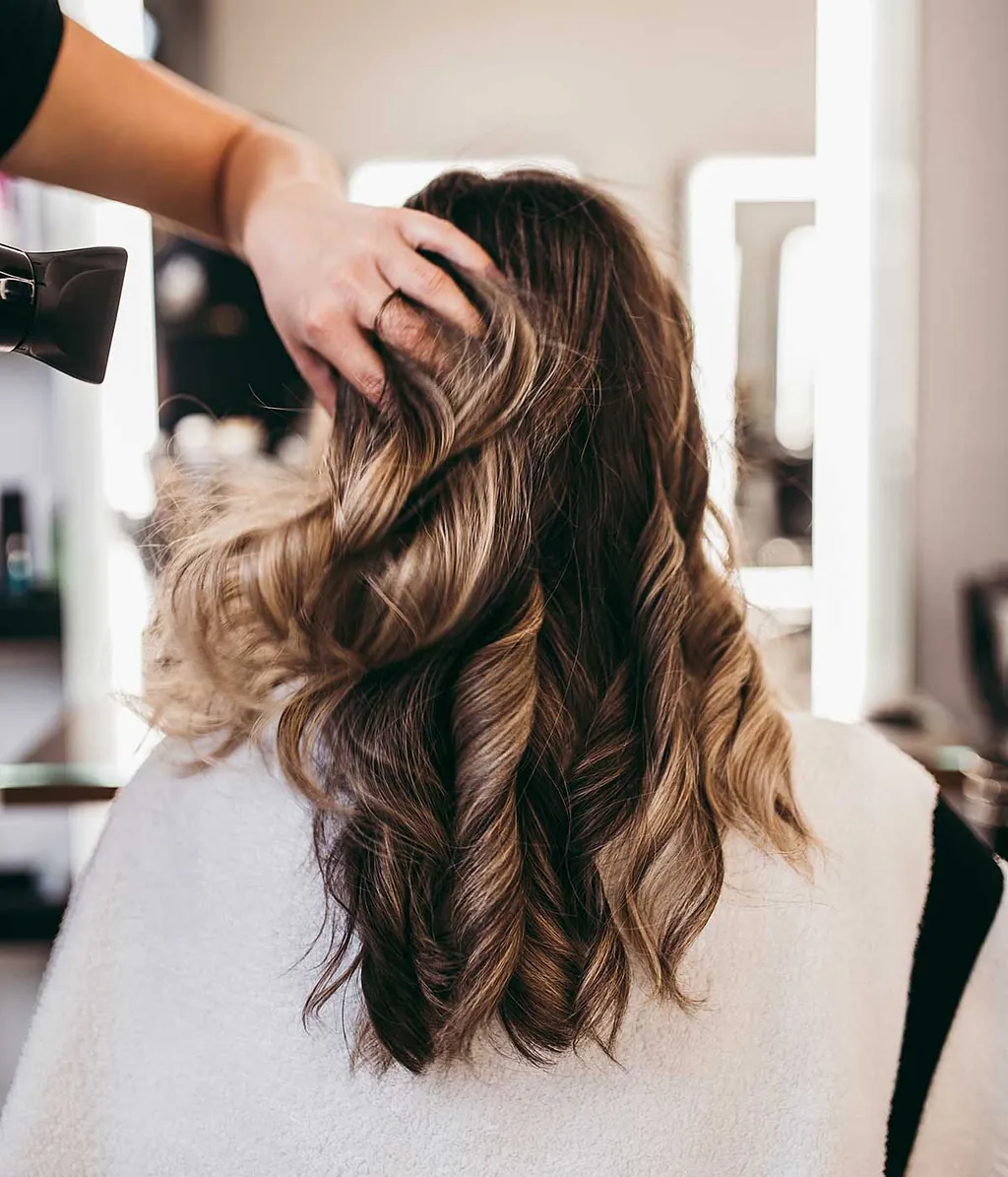 Schöne brünette Frau mit langen Haaren im Schönheitssalon, die sich die Haare bläst.